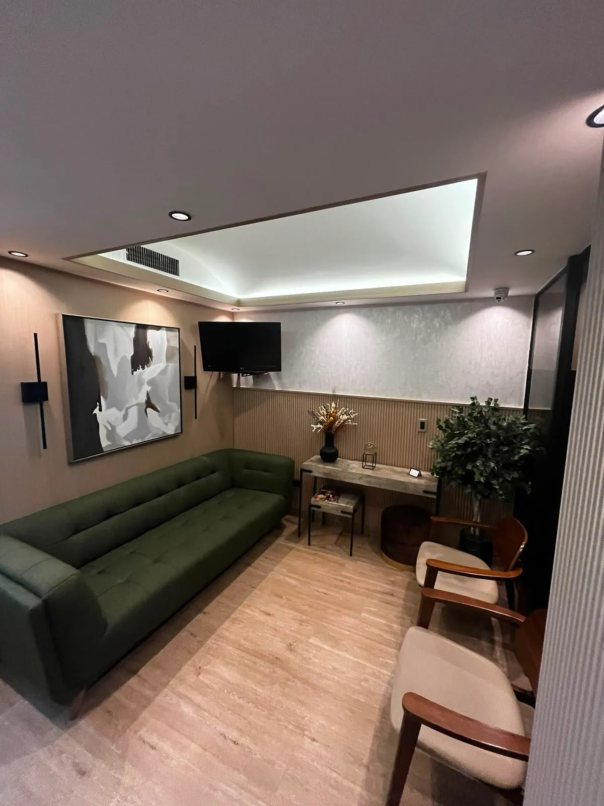 Lounge de espera de la sucursal Piantini con sofá verde, obra de arte y televisor