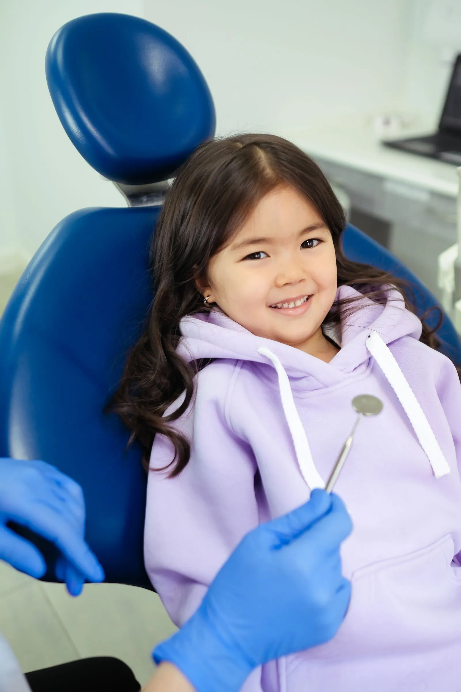 Niña sonriendo sentada en el sillón dental mientras la odontóloga prepara el espejo
