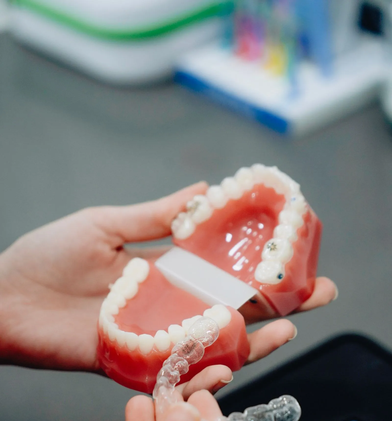 Manos sosteniendo un modelo de arcada con brackets y un alineador transparente