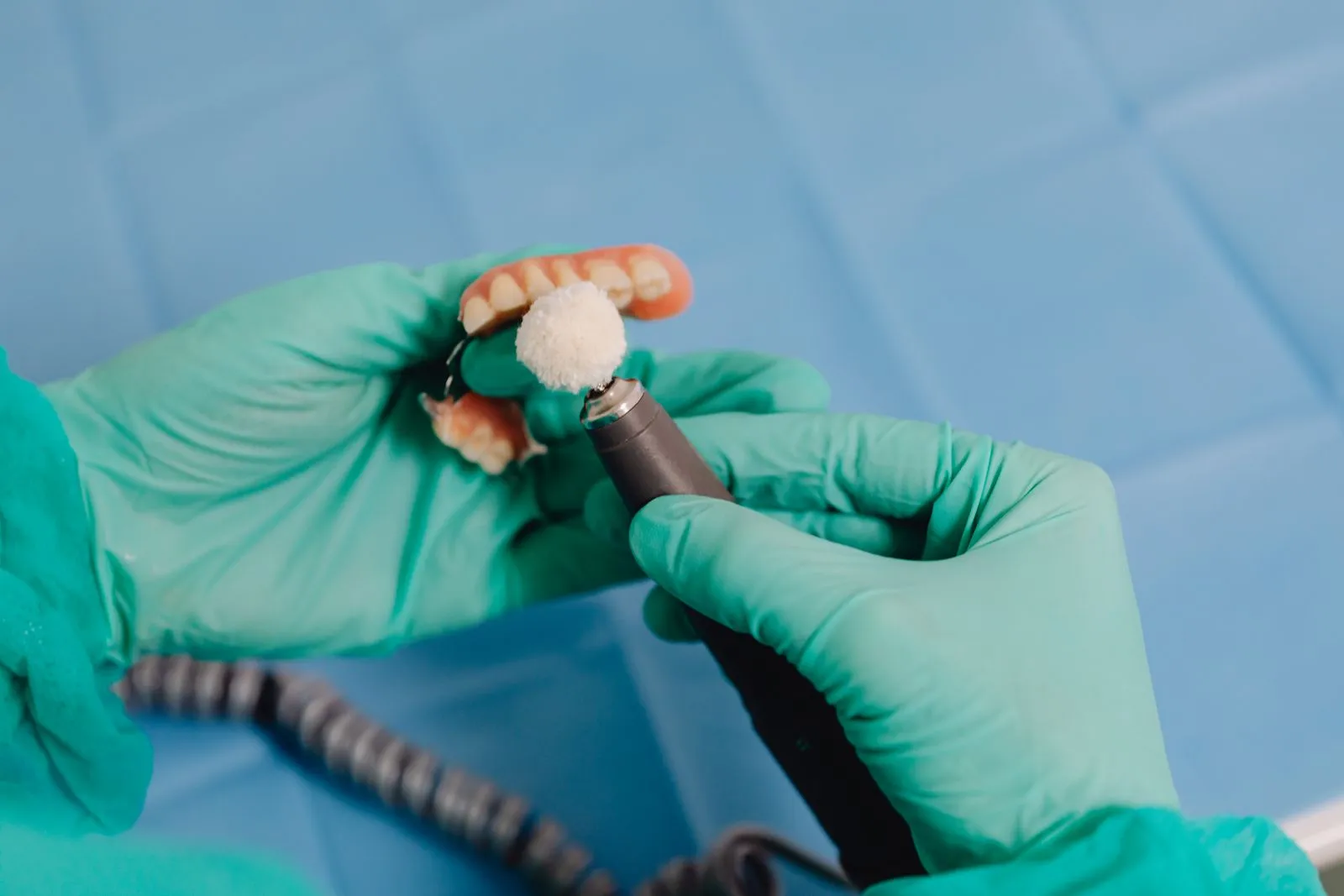 Técnico con guantes verdes puliendo una prótesis dental parcial